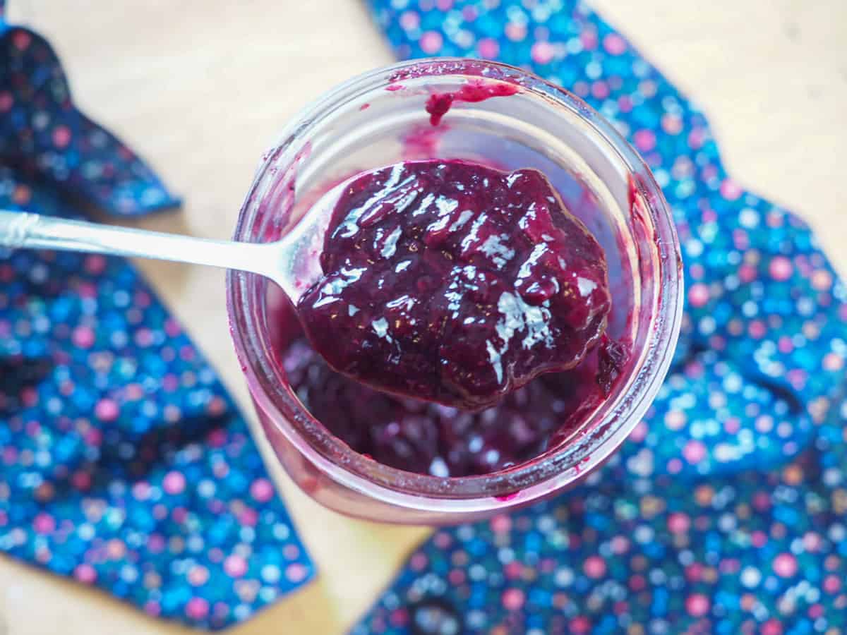 A spoon of paleo blueberry jam in a large jar.