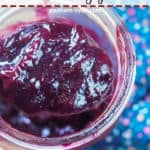 A pin image of a spoon scooping paleo blueberry jam out of a large jar.