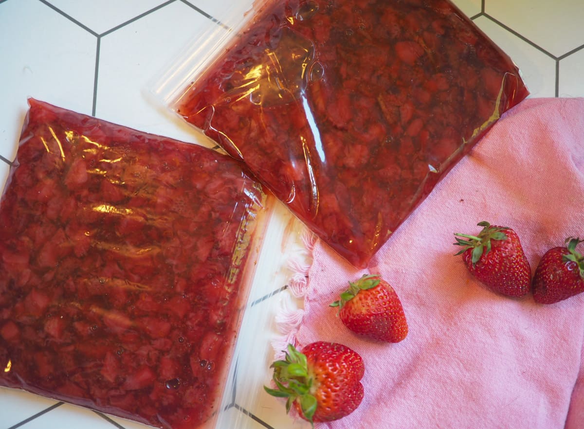 Two bags of strawberry jam on a white tile floor.