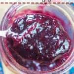 A pin image of a spoon of blueberry jam in a large jar.