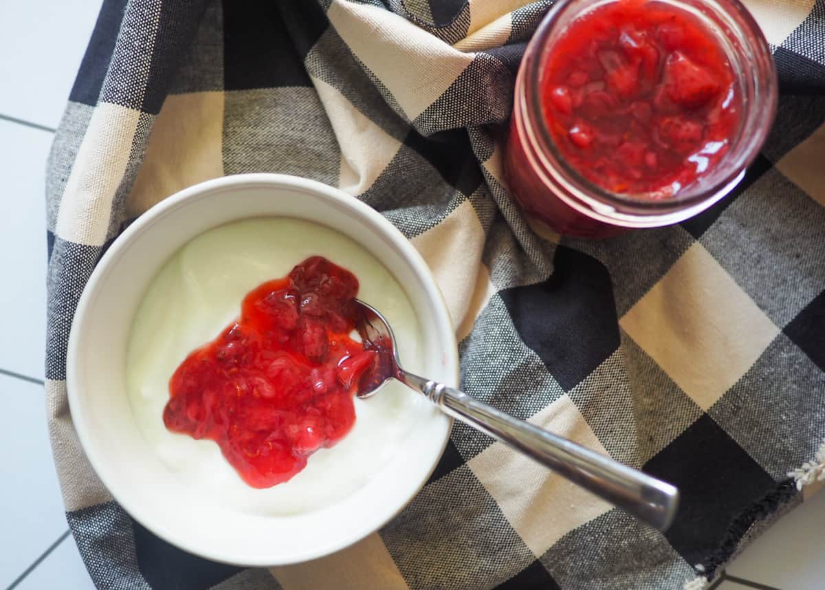 A white bowl of yogurt with paleo strawberry jam on top and a jar of strawberry jam on the side.