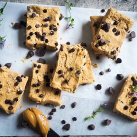 Peanut butter and chocolate chip perfect bars on a piece of parchment paper with a knife and a glob of peanut butter.