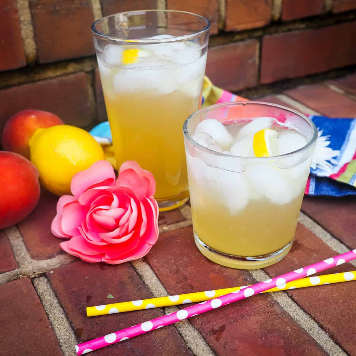 Two glasses of peach lemonade on brick steps with colored straws and lemon slices.