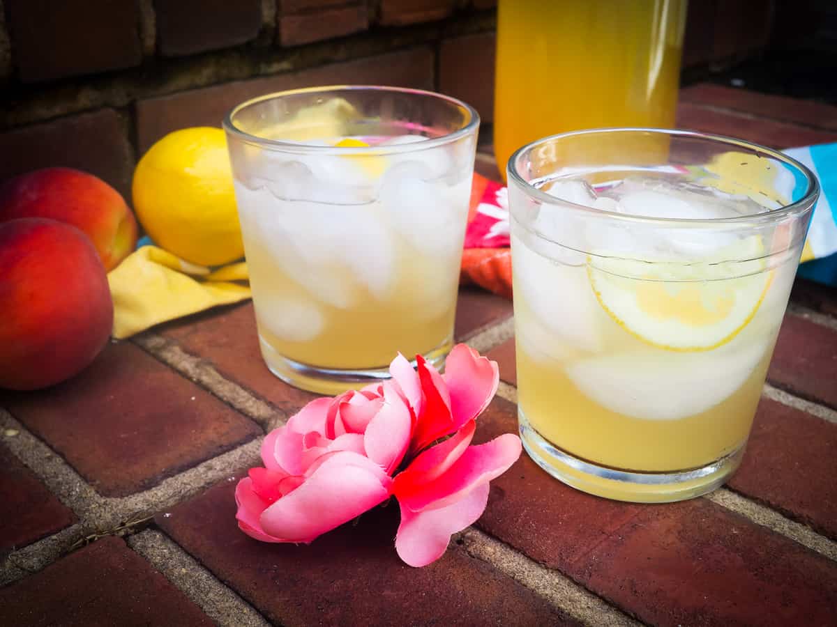 Two glasses of peach lemonade with a pink flower on brick stairs.