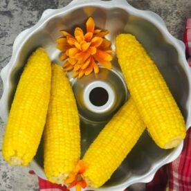 four cooked ears of corn in a silver bowl with orange flowers