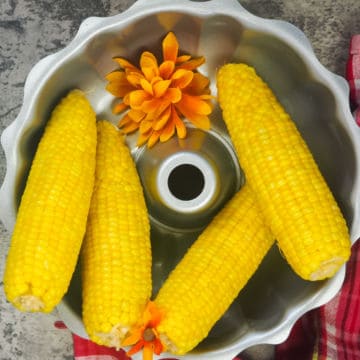 four cooked ears of corn in a silver bowl with orange flowers