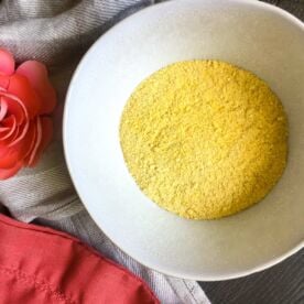 a white bowl of homemade cornmeal with a pink flower and a linen towel