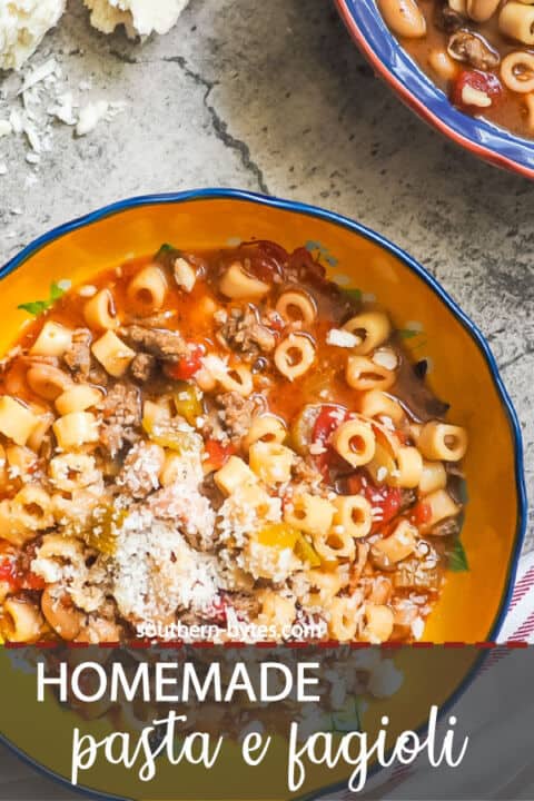 a pin image of two blue bowls of pasta e fagioli and a block of parmesan cheese.