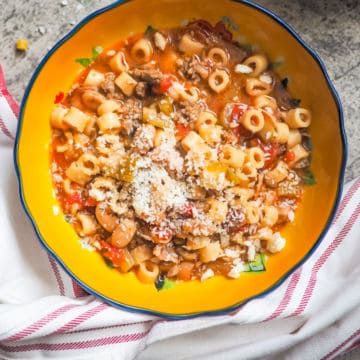 A yellow bowl of pasta e fagioli on a gray background.