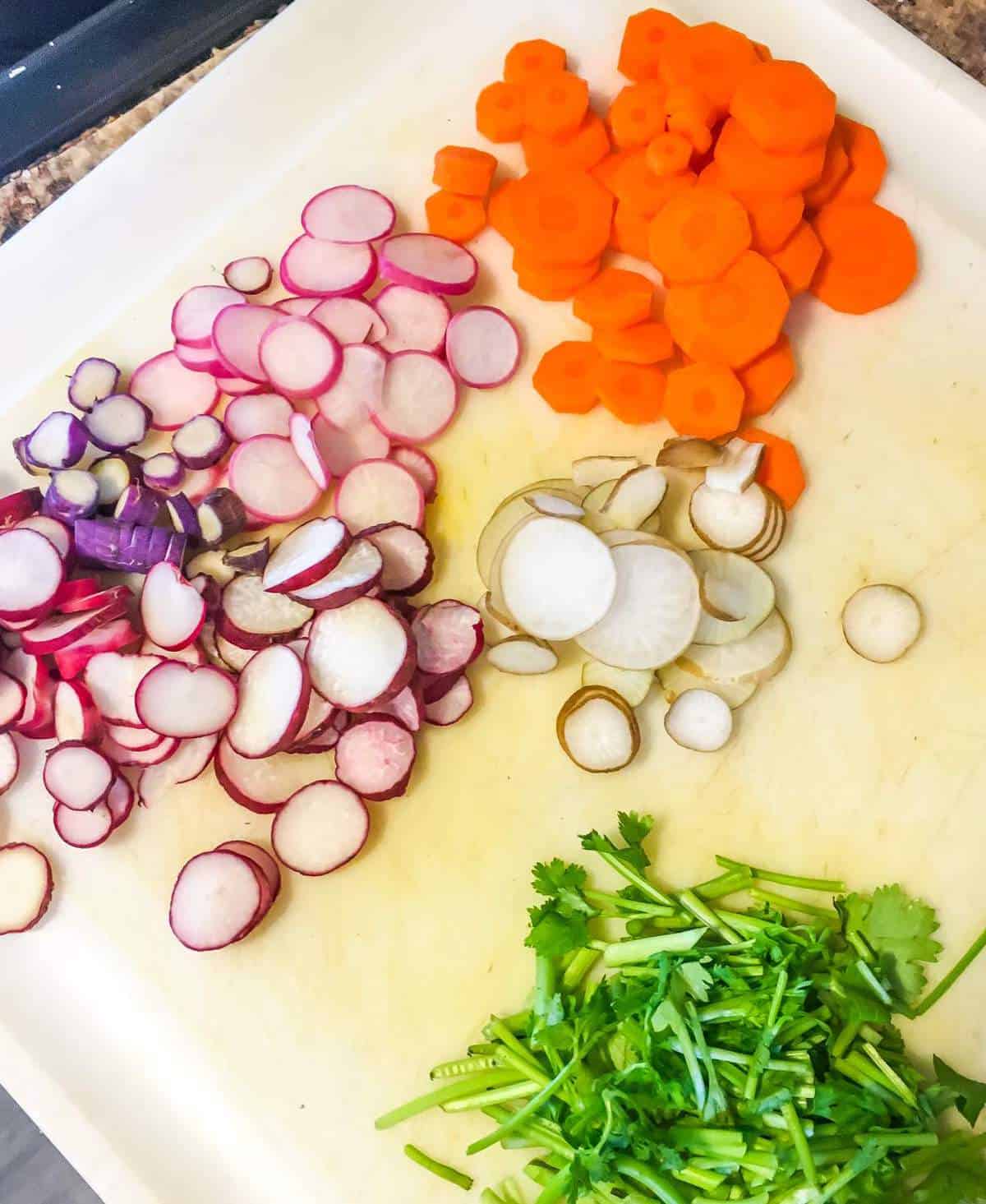 sliced radishes and carrots on a white cutting board