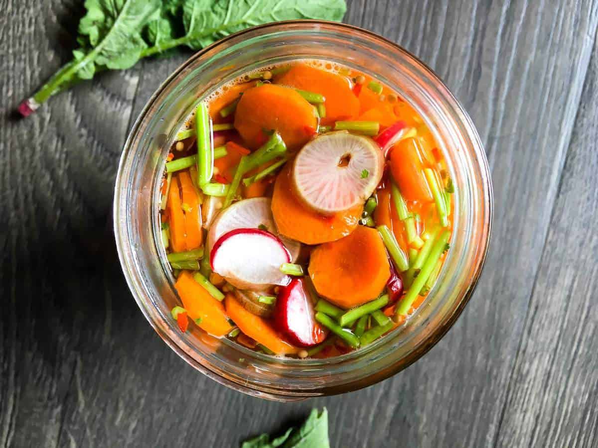 an overhead image of a jar of pickled carrots and radishes