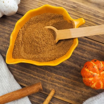 A yellow bowl shaped like a leaf with pumpkin pie spice seasoning in it and a small wooden spoon.