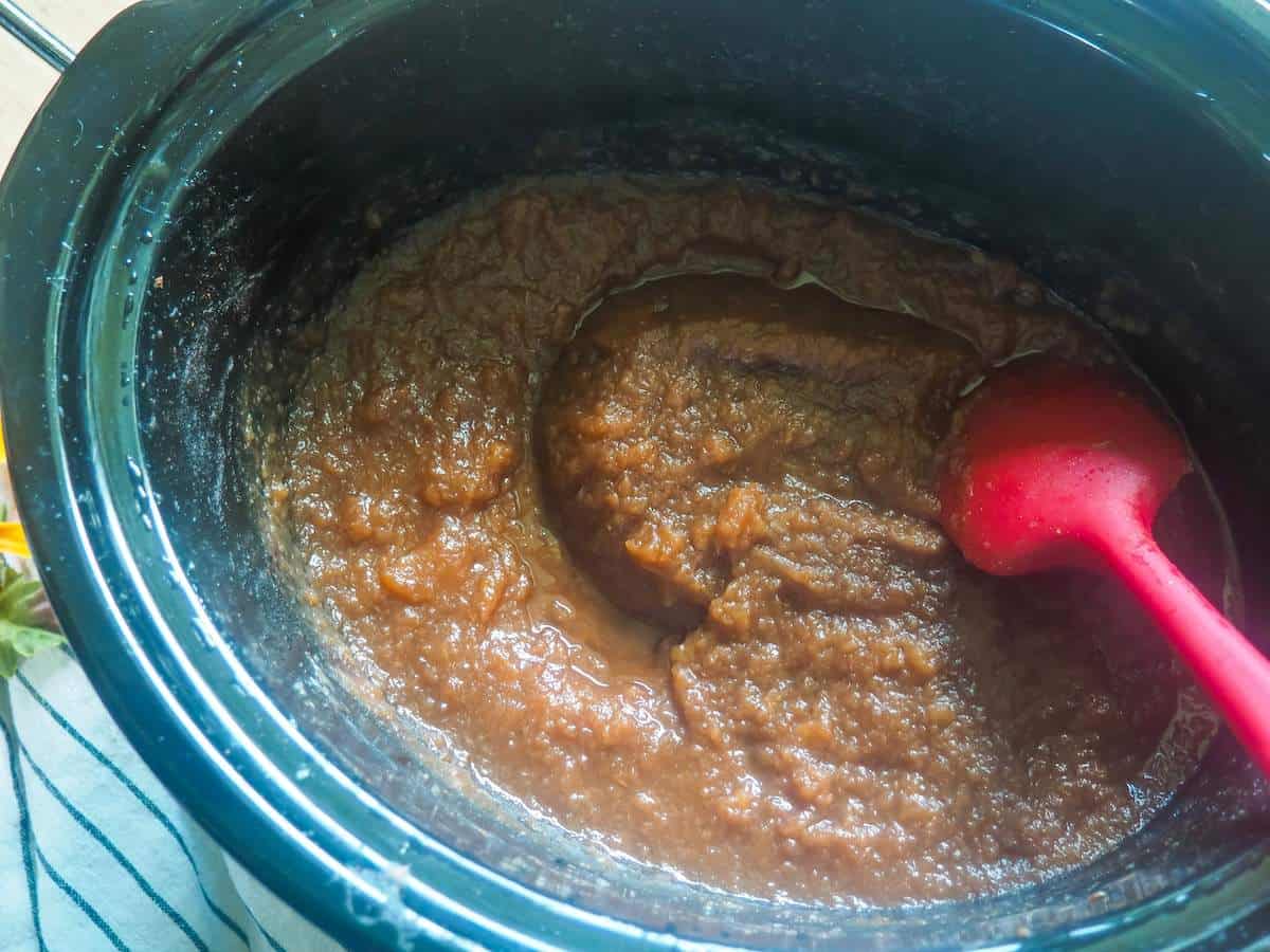 A crockpot with cooked apple butter in it.