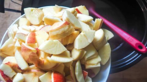A bowl of sliced apples being dumped in a crock pot.