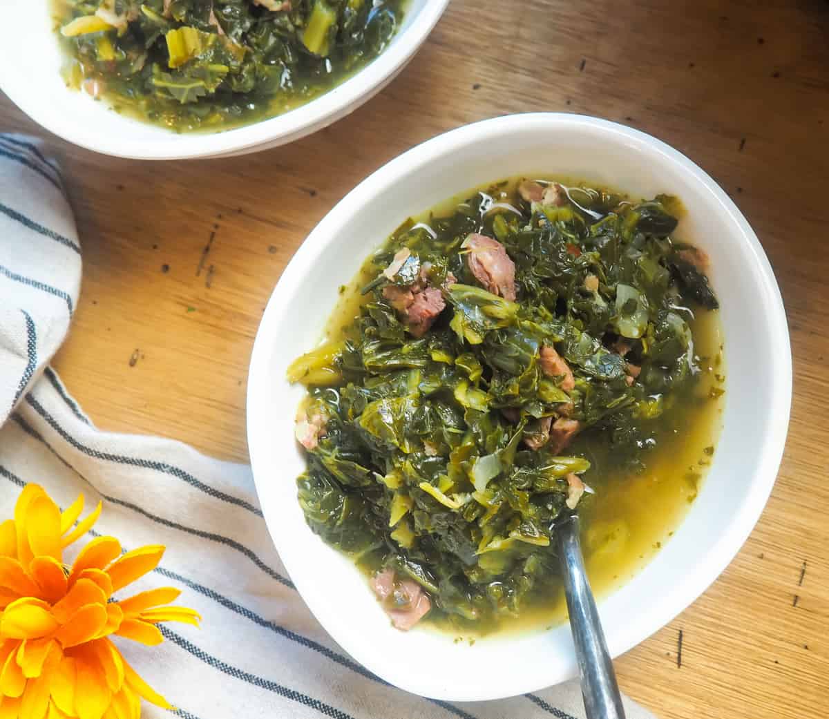 a white bowl of collard greens with bits of ham and bacon