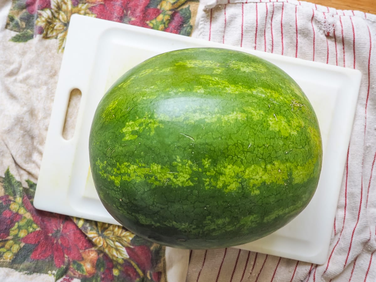 A whole watermelon on a white cutting board.