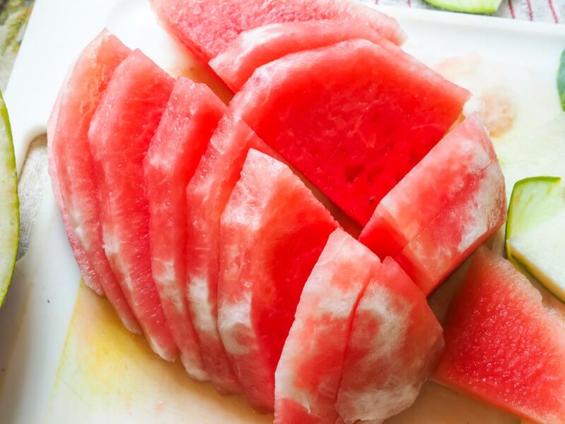 Large cut up slices of watermelon on a white cutting board.