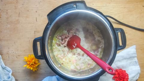 an instant pot with bacon, ham, onions, and broth in it.