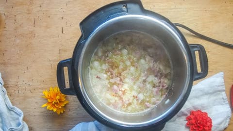 an instant pot with bacon, ham, onions, and broth bubbling in it.