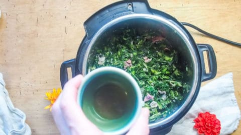 apple cider vinegar being poured into an instant pot of collard greens.