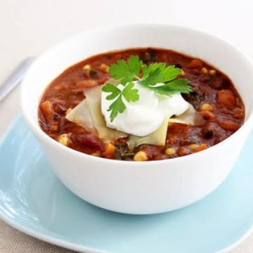 A bowl of three bean and sweet potato chili with a dollop of sour cream on top.