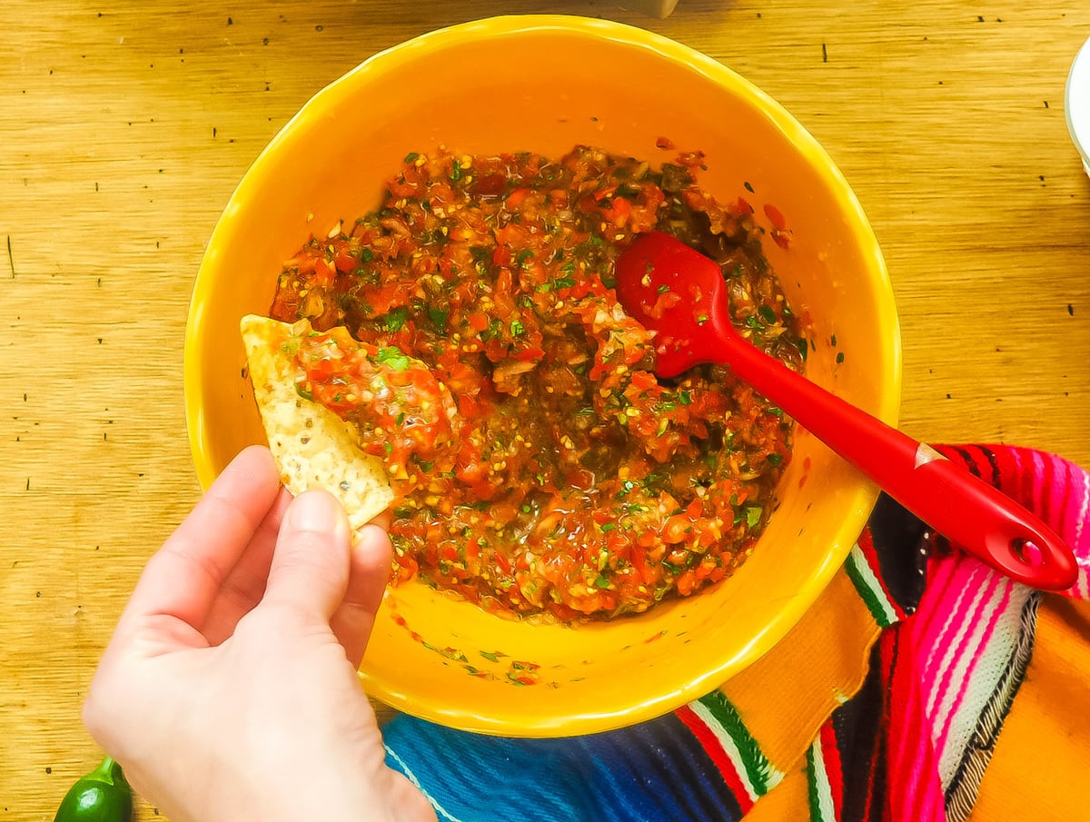A yellow bowl of cherry tomato salsa and a chip scooping some out.