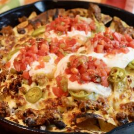 A cast iron skillet filled with nachos topped with jalapeños and salsa.
