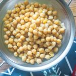 A zoomed in image of cooked chickpeas in a metal strainer with a blue napkin.