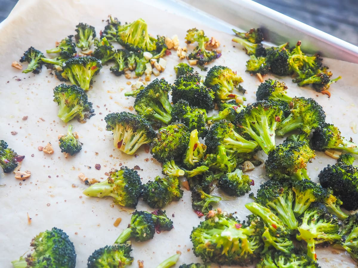 A cookie sheet with roasted broccoli and garlic on it.