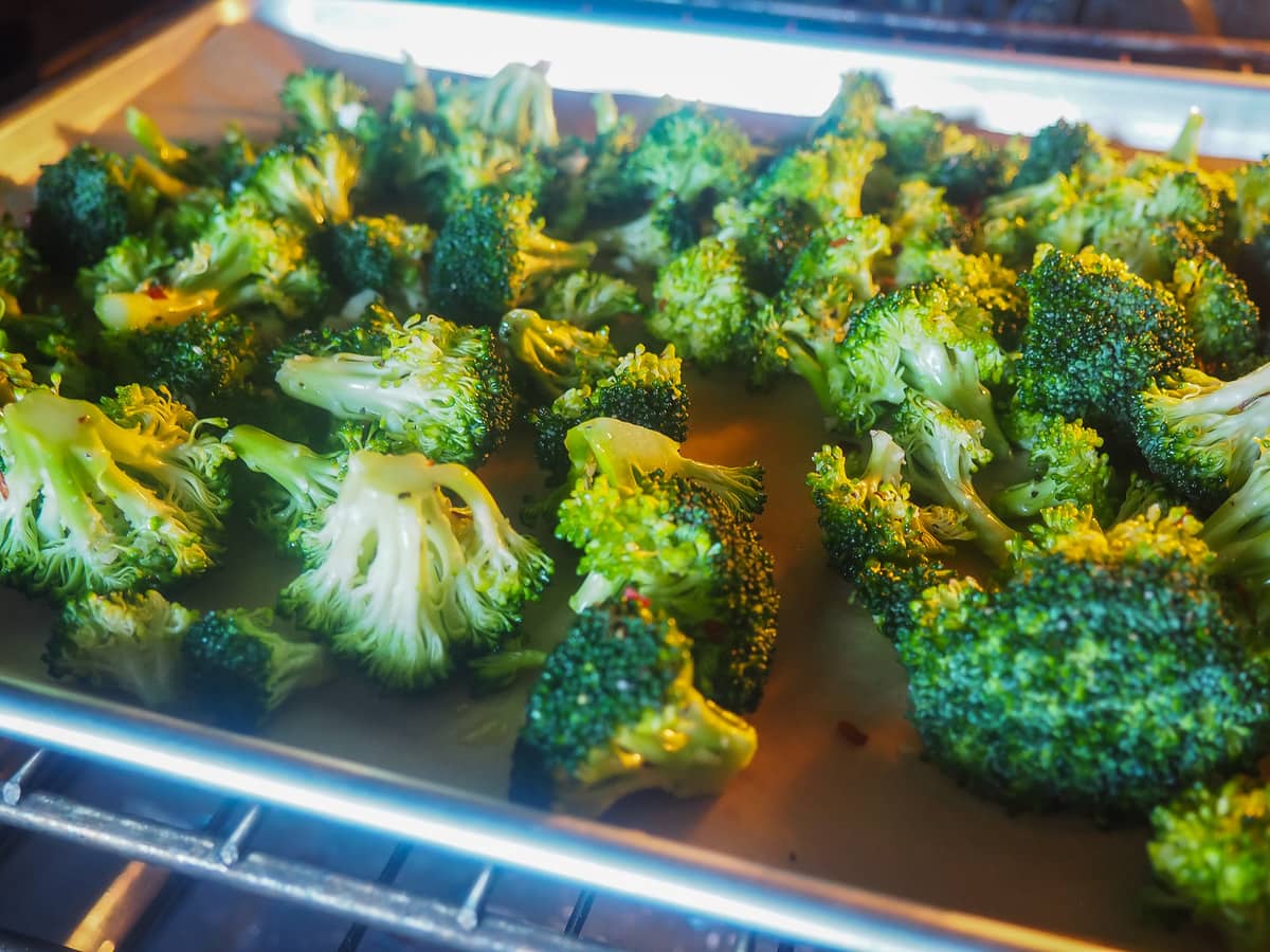 A cookie sheet in the oven with broccoli roasting on it.