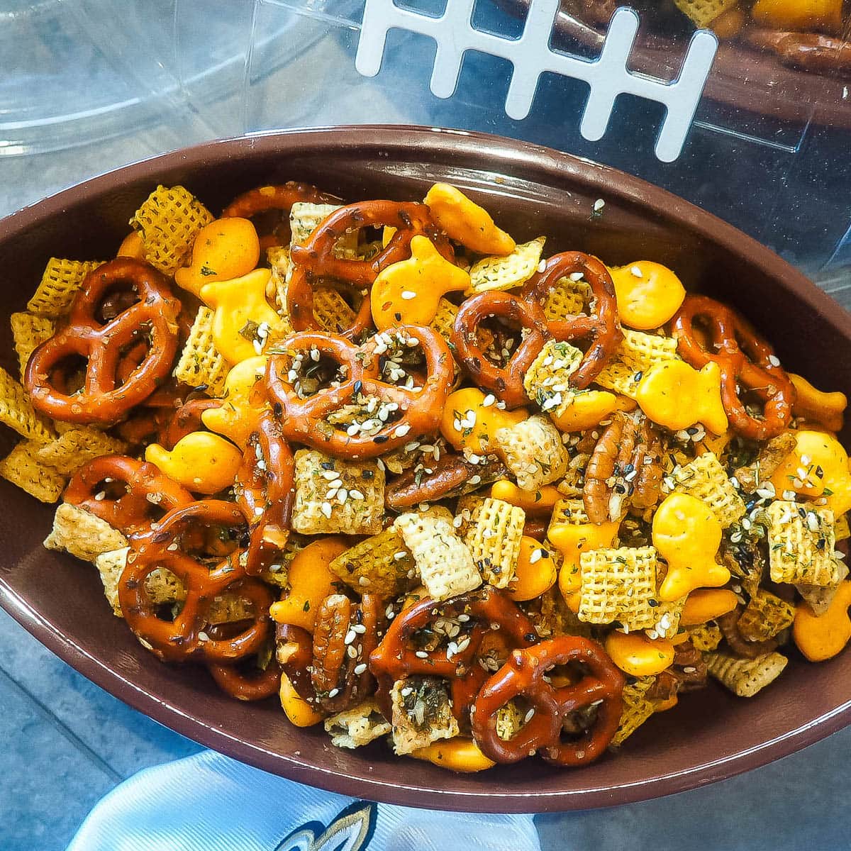 A football shaped bowl of chex party mix with pretzels, chex, and goldfish.