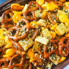 A close-up of a football shaped bowl of party mix with pretzels, chex, and goldfish.