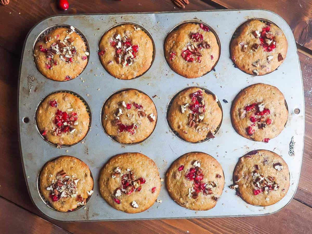 Freshly baked cranberry orange muffins sprinkled with pecans still in the muffin tin.