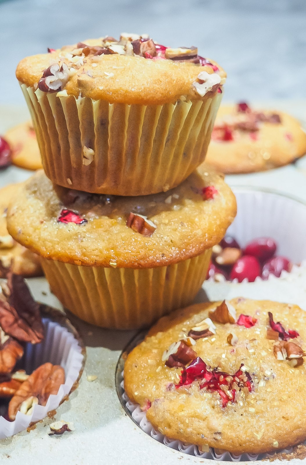Freshly baked cranberry orange muffins sprinkled with pecans stacked on top of a muffin tin.