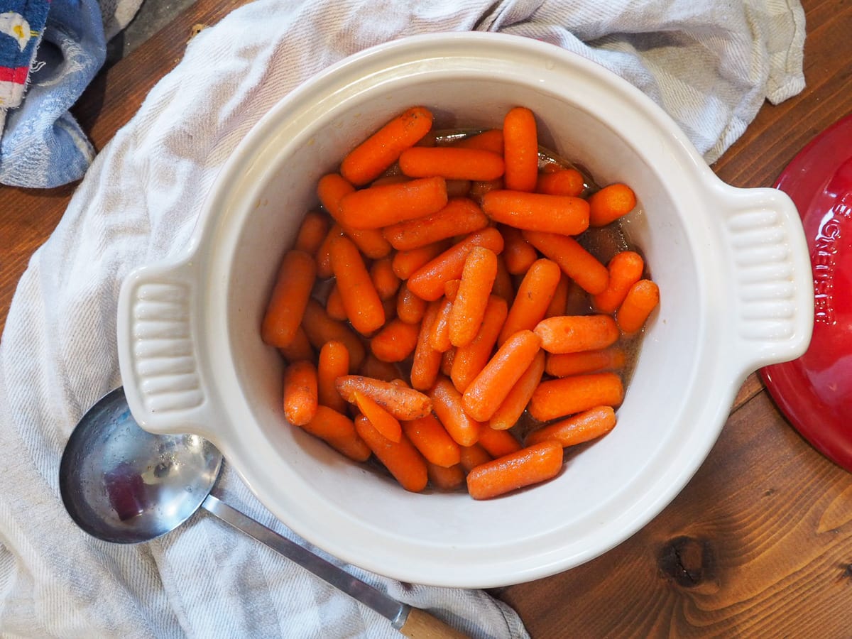 Glazed carrots in a white serving dish with a serving spoon.