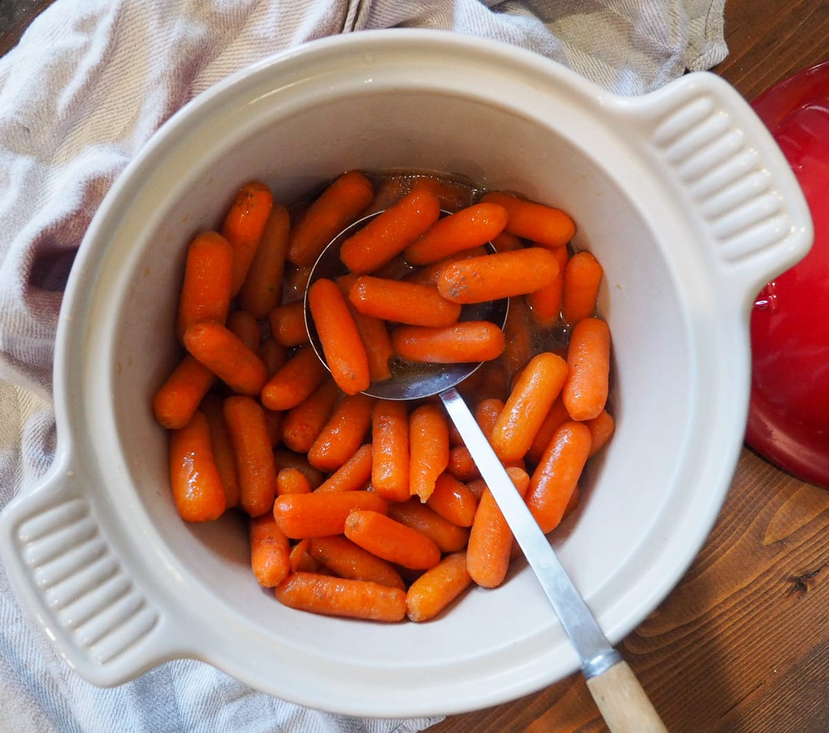 Glazed carrots in a white serving dish with a serving spoon.