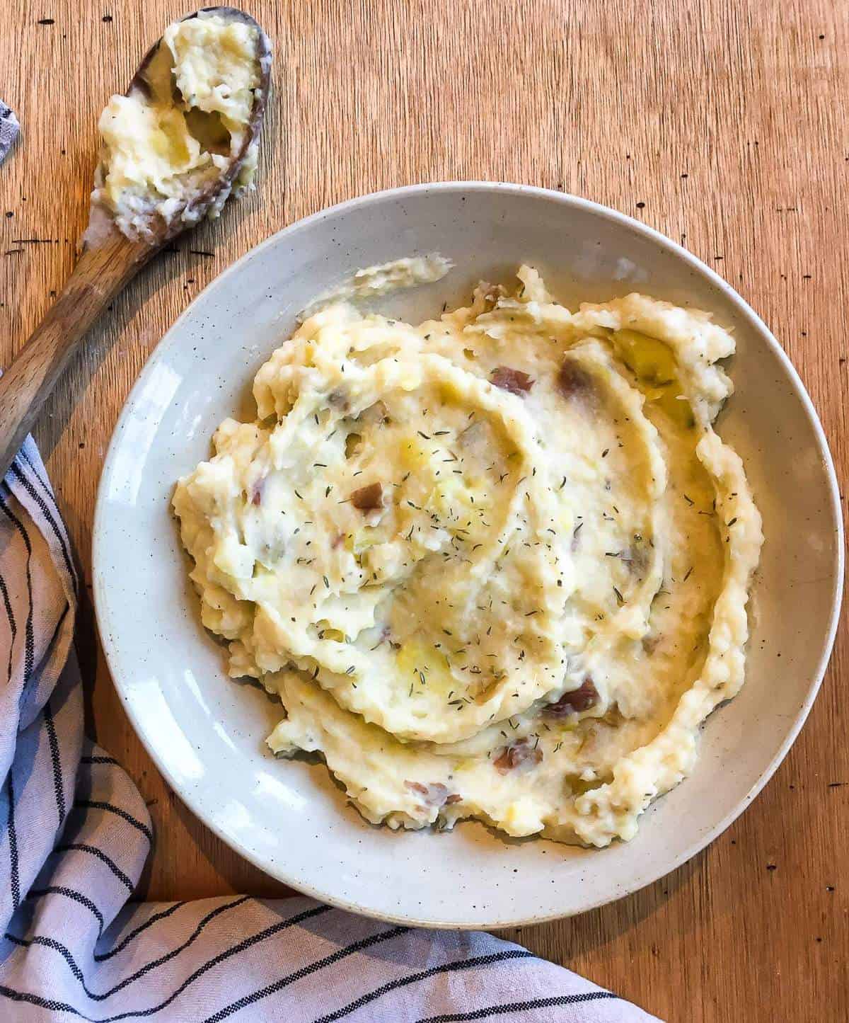 A bowl of cheesy garlic mashed potatoes and a wooden spoon.