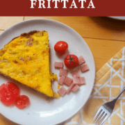 A pin image of a slice of ham and gruyere frittata with some fresh tomatoes on a white plate.