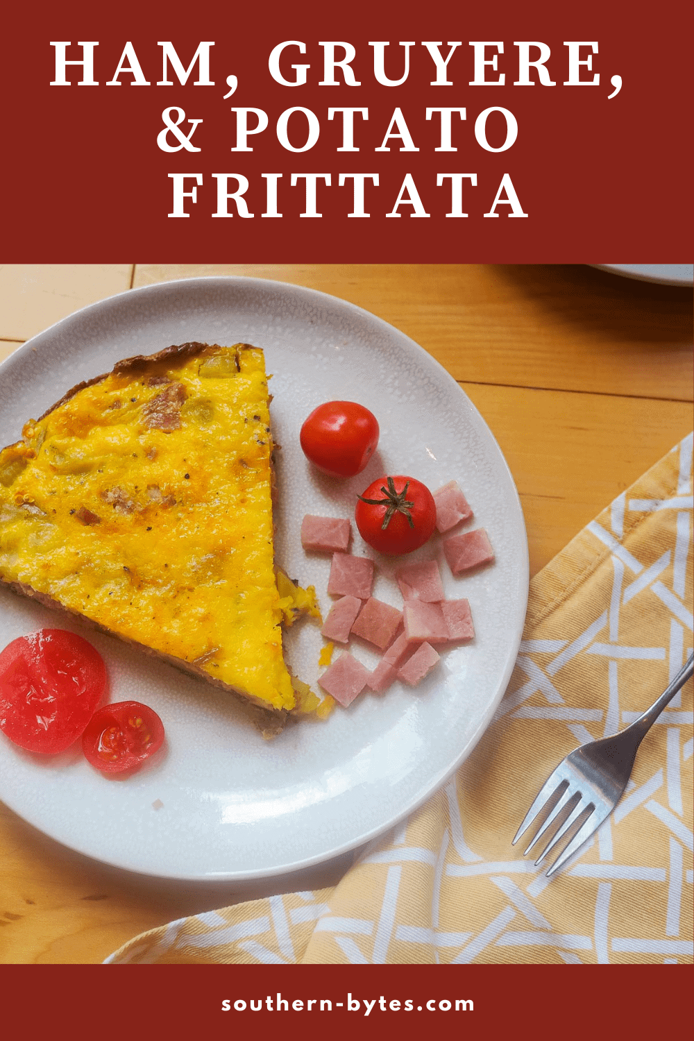 A pin image of a slice of ham and gruyere frittata with some fresh tomatoes on a white plate.