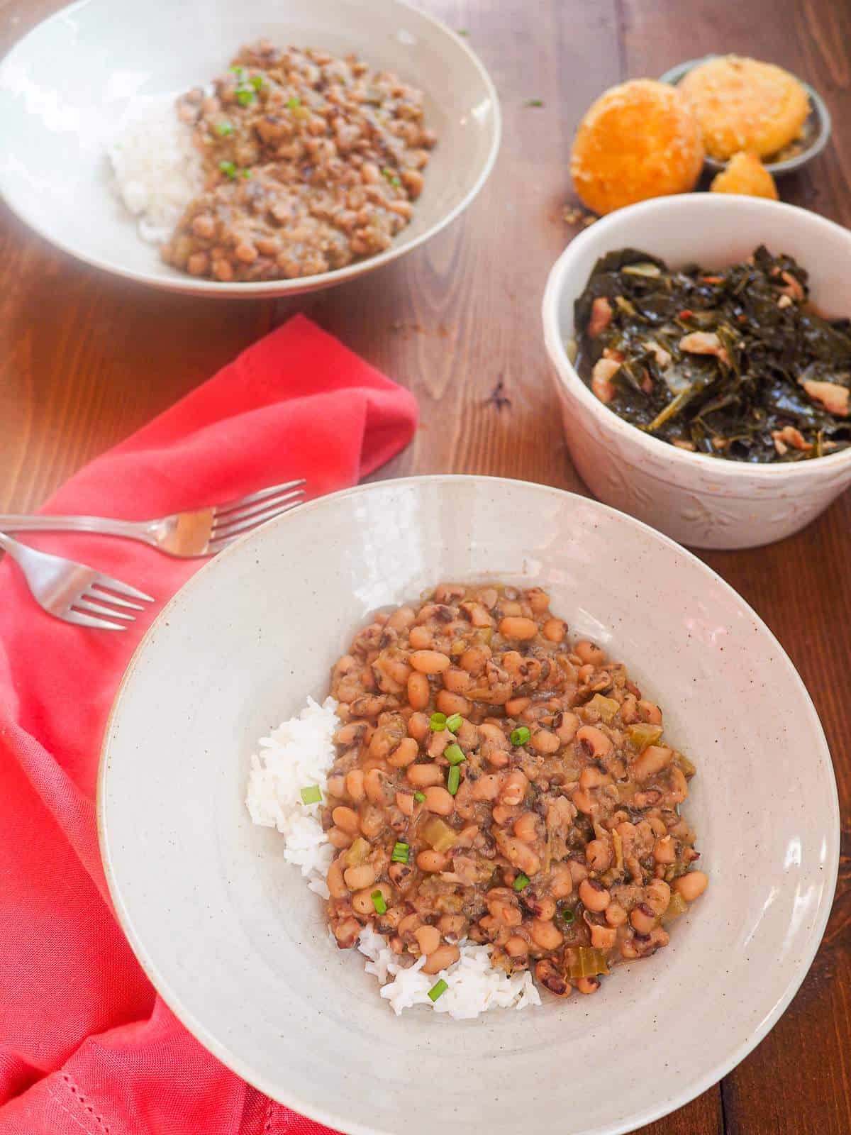 Two bowls of hoppin john black eyed peas with a bowl of collard greens and some corn muffins.
