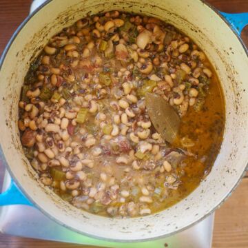 A blue pot half filled with cooked hoppin john black eyed peas.