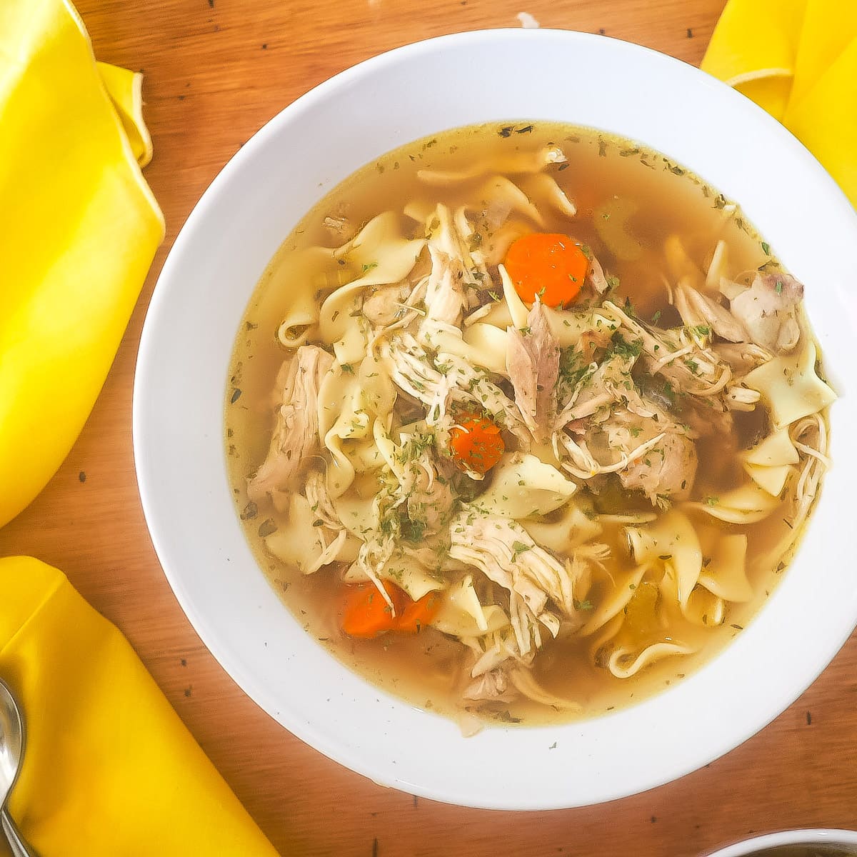 A white bowl of chicken noodle soup with yellow napkins.