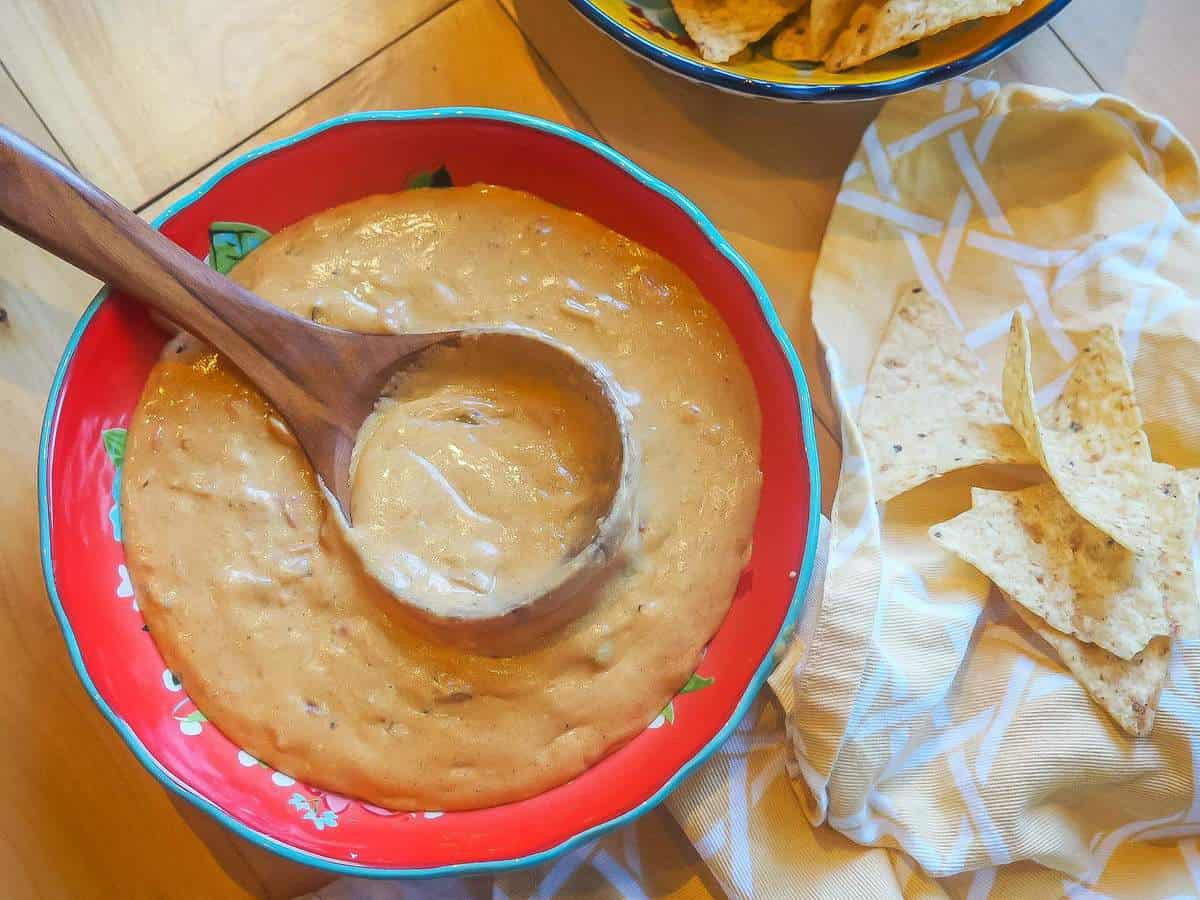A red bowl filled with instant pot queso with chips and a wooden spoon.