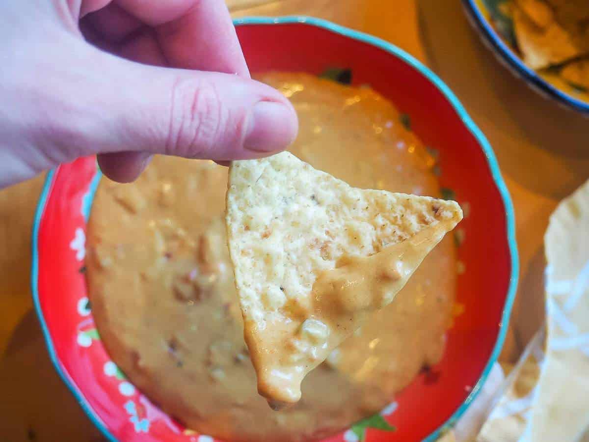 A chip dipped in queso held over a red bowl.