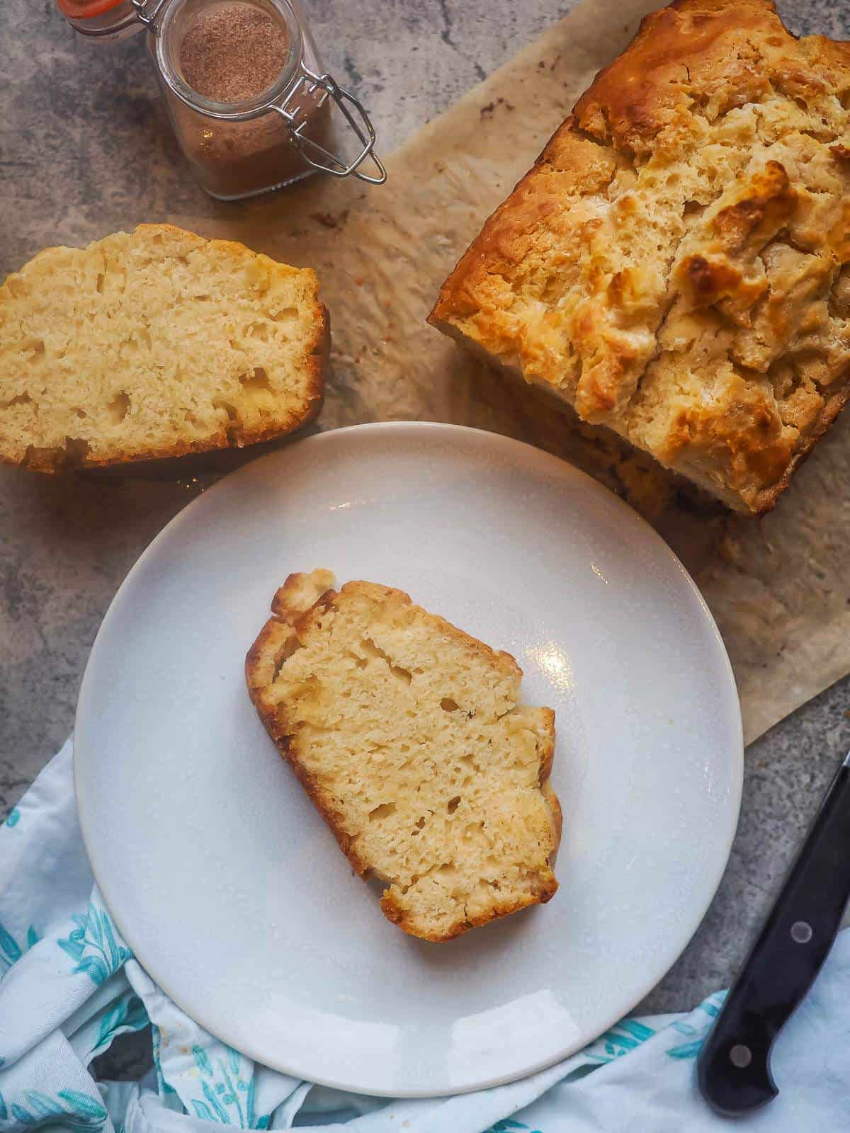 A slice of beer bread on a white plate next to the rest of the loaf.