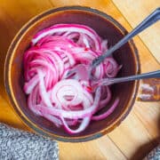 A small brown mug with pickled red onions and two small forks twisted in the onions.