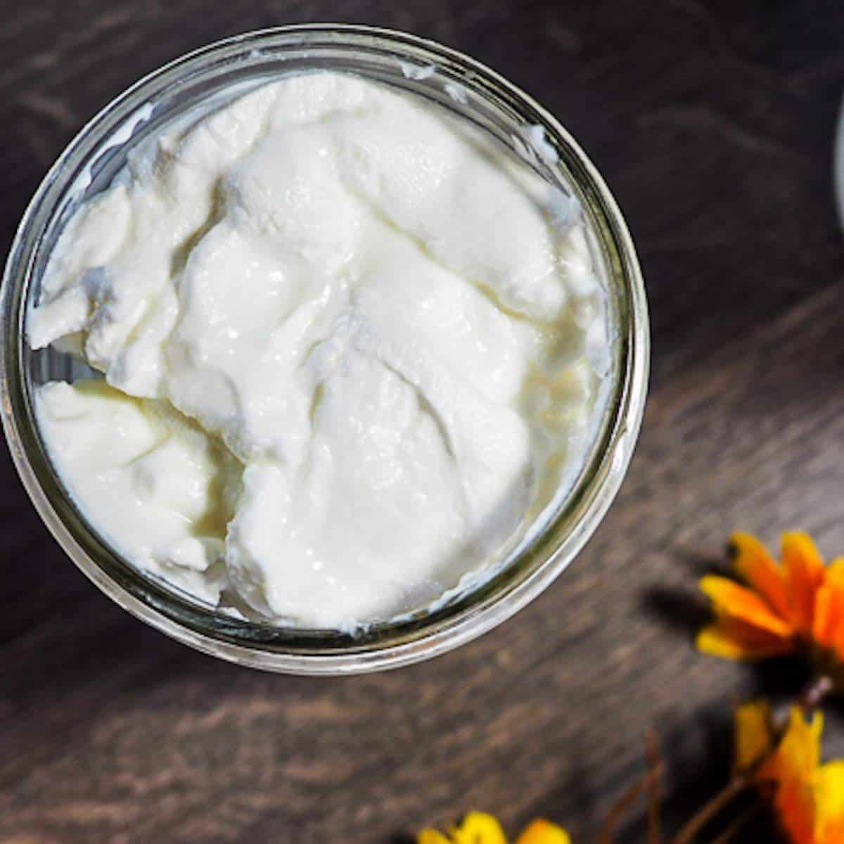 A mason jar full of homemade yogurt and a yellow flower on a gray wood background.