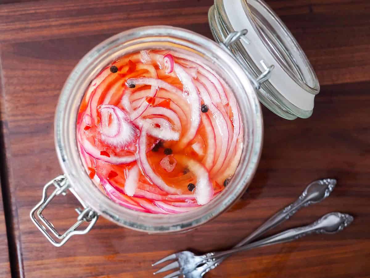 A glass jar with pickled red onions in it and two small forks on the side.