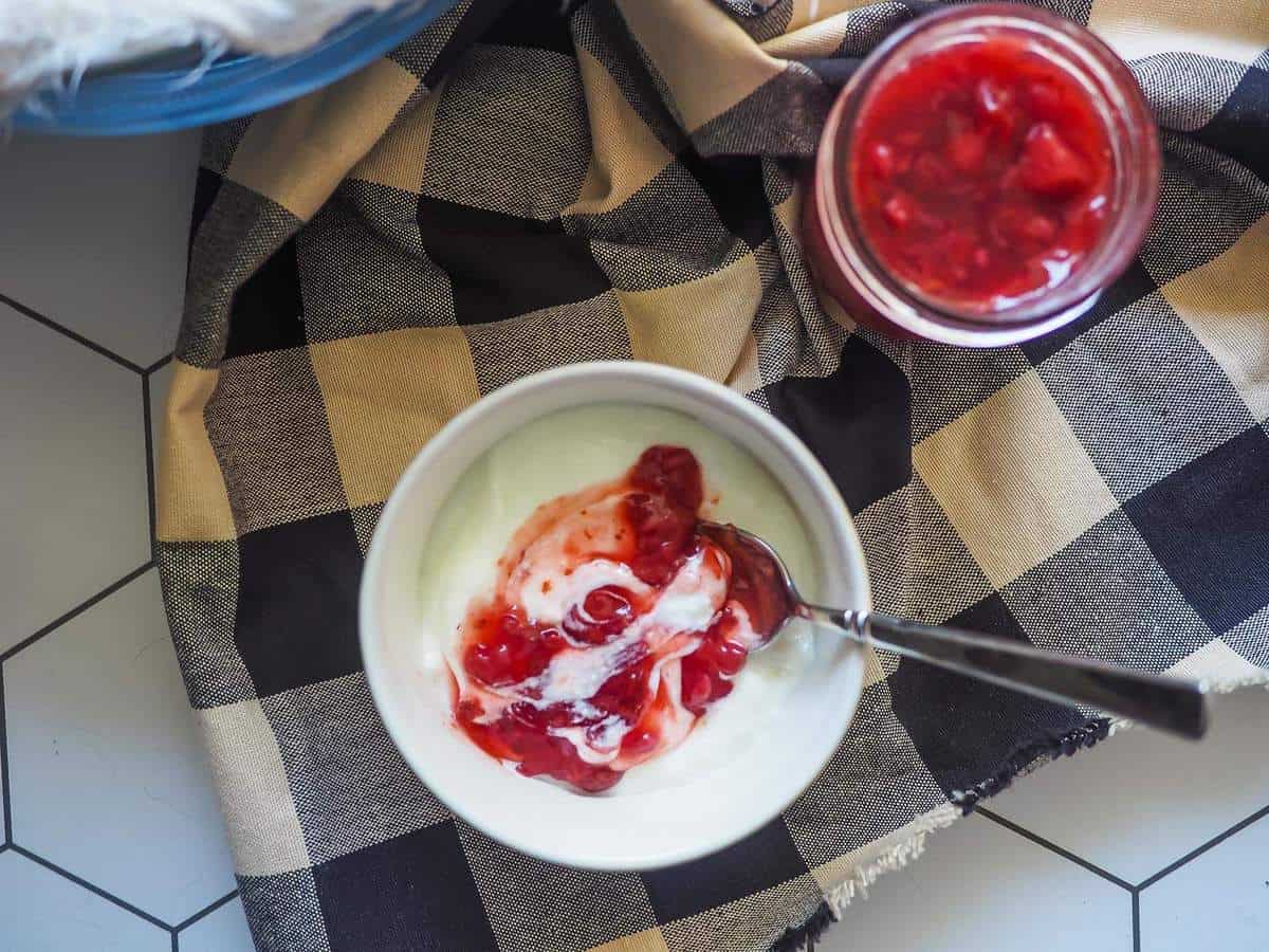 A white bowl of yogurt with paleo strawberry jam on top and a jar of strawberry jam on the side.