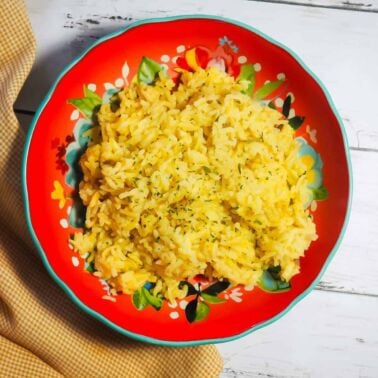 A red bowl of rice pilaf on a wood board with a yellow napkin.